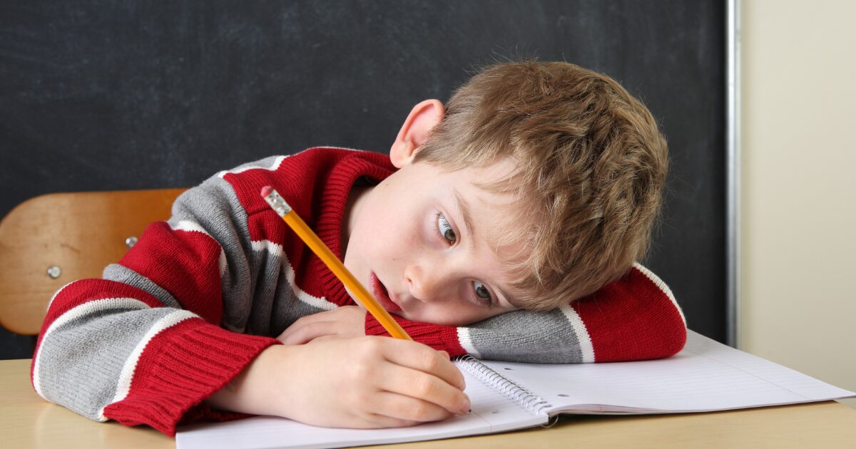 boy bored of schoolwork, writing on his notebook with a pencil